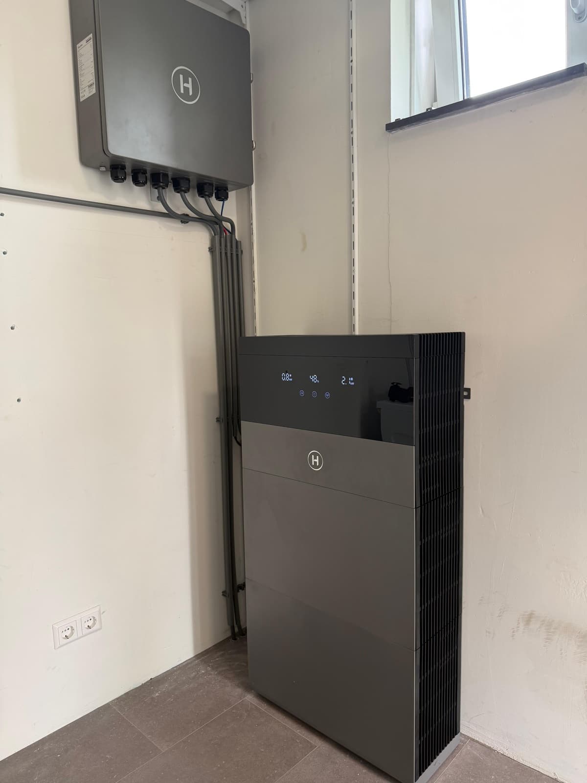 Donkere Hoymiles-thuisbatterij met omvormer aan de wand in een bijkeuken met tegelvloer