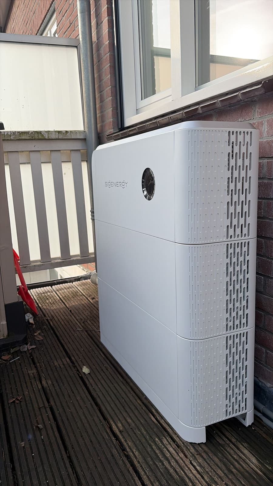 SigenStor-thuisbatterij buiten op een houten balkon tegen de gevel, onder een raam