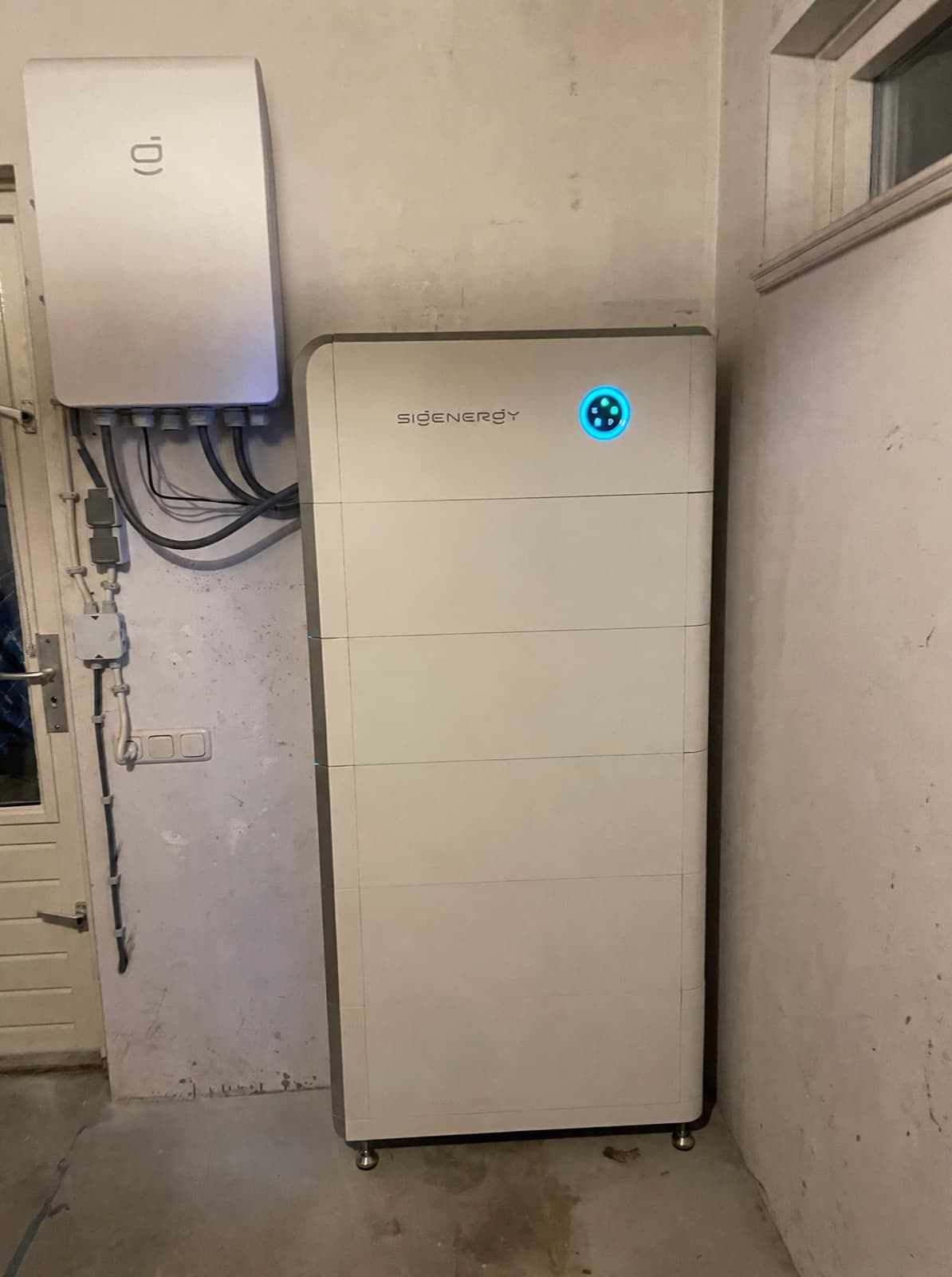 SigenStor-thuisbatterij met blauw verlichte bedieningsring naast een wandomvormer in een garage